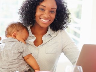 Mother holding baby while doing schoolwork